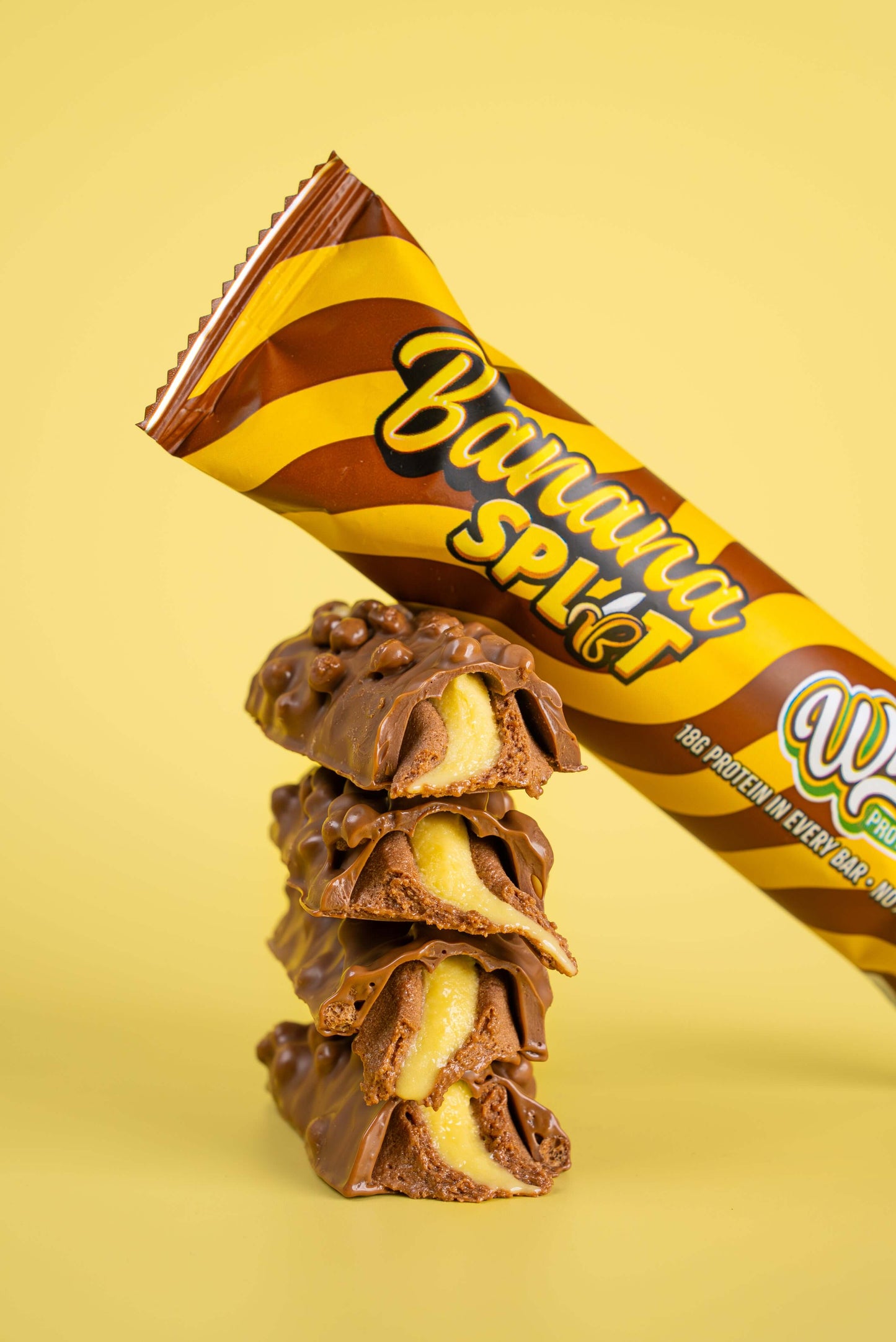 Wispy Eiwitreep verpakking in de smaak banana split leunend tegen opengesneden repen waar van je de binnenkant ziet